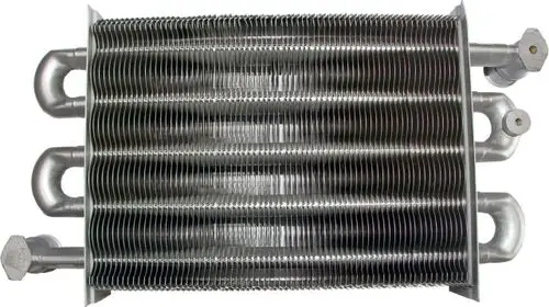 Heizwasserwärmetauscher aus Metall mit mehreren Röhren und Anschlüssen, verwendet in Heizsystemen, sichtbar montiert, möglicherweise von der Marke Wolf.